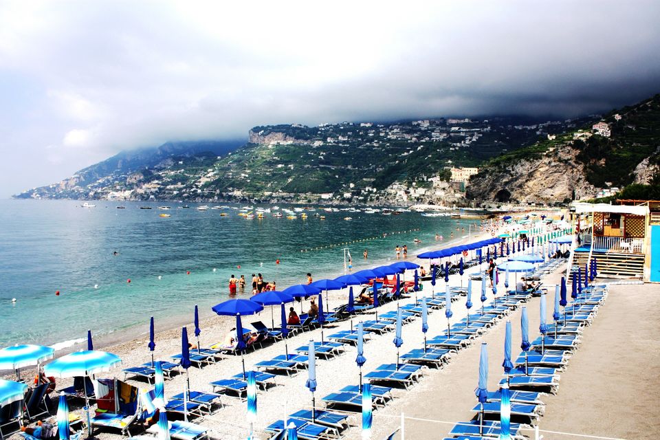File di ombrelloni sulla spiaggia di Maiori, con il mare e le case sui pendii della Costiera