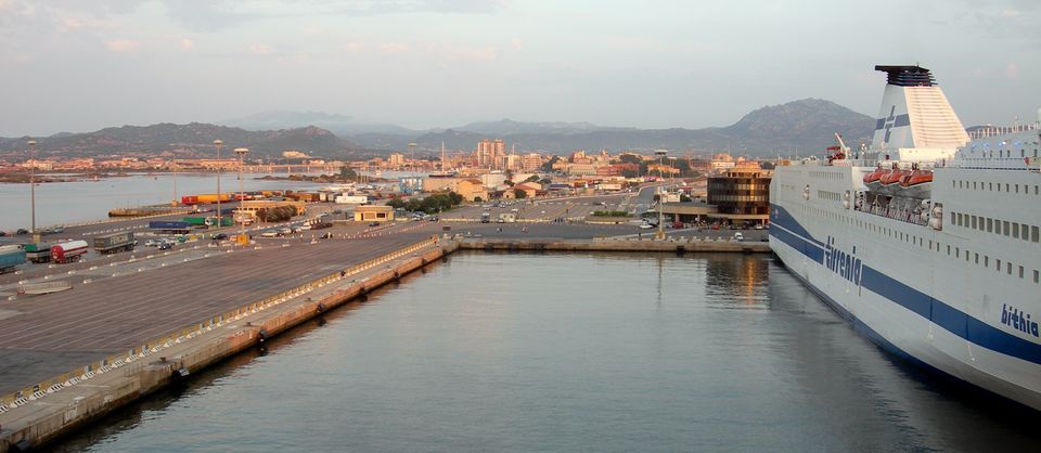 Un traghetto ormeggiato nel porto di Olbia, con i piazzali d'imbarco, la città e le colline sullo sfondo
